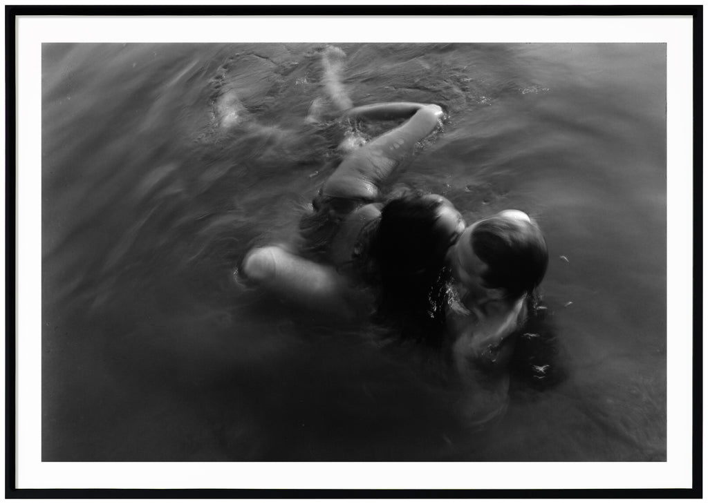 Analogous photograph of a woman and man hugging in water.  Black frame. 