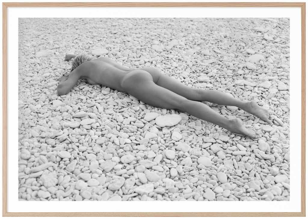 Black and white photograph of a naked woman lying on beach with white stones. Oak frame. 