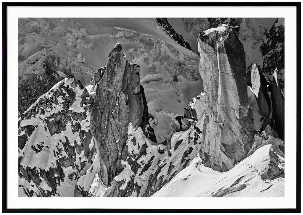 Black and white photograph of steep cliffs partly covered by snow.  Black frame. 