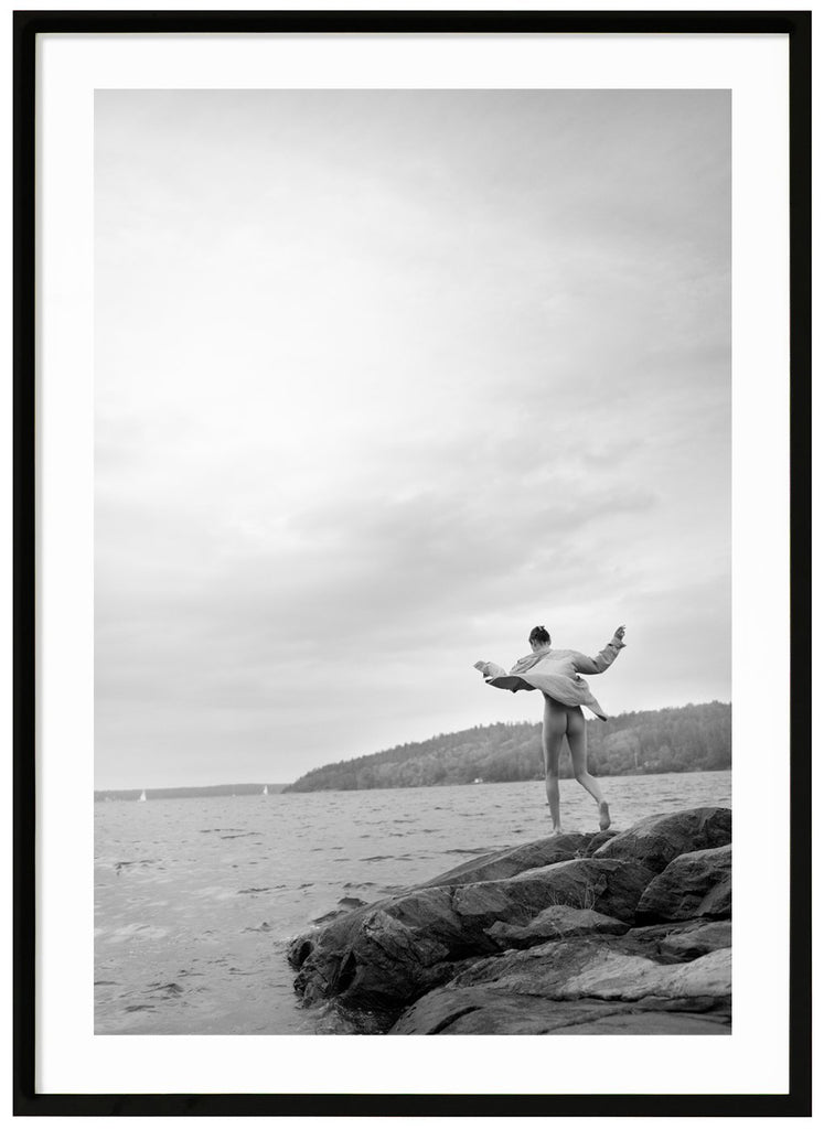 Black and white photograph of a woman on rocks in the archipelago. Black frame. 