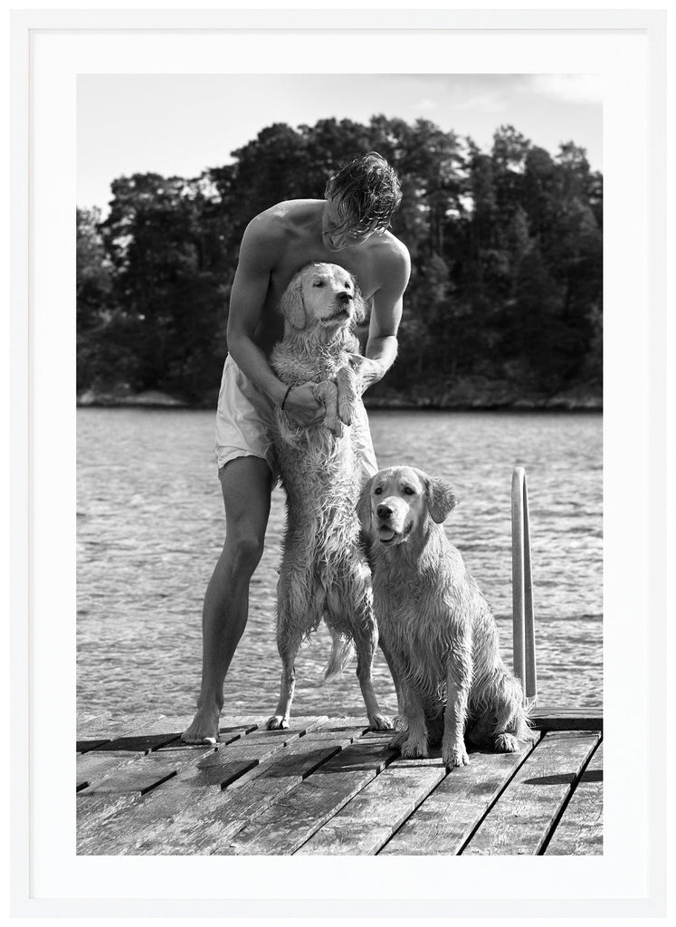 Black and white poster of guy with dogs on a wet jetty. Portrait format. White frame. 