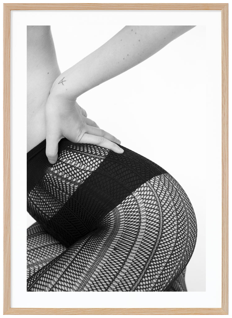 Black and white poster of sitting woman wearing black panties and fishnet tights. Portrait format. Oak frame. 