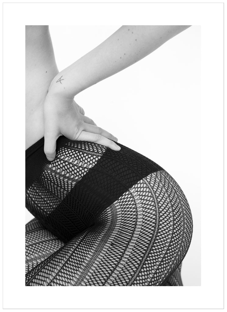 Black and white poster of sitting woman wearing black panties and fishnet tights. Portrait format.