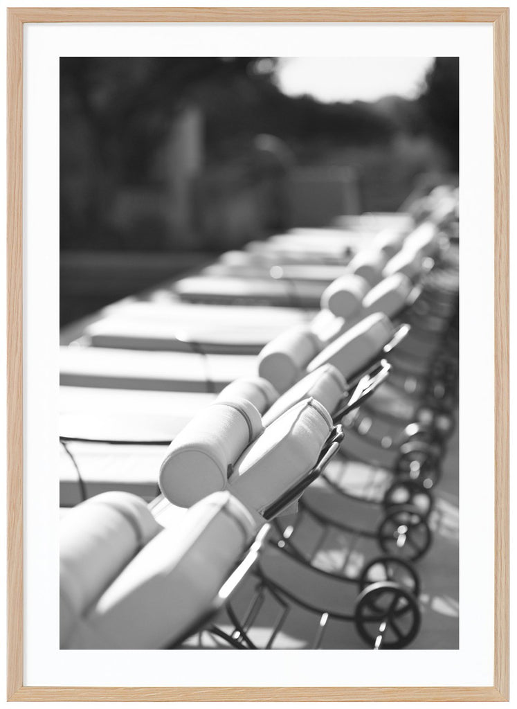 Black and white photograph of several lined up white sun loungers in the sun. Oak frame.