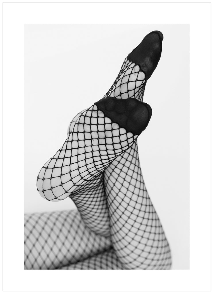 Black and white photograph of a woman's legs with her feet angled towards the camera, she is wearing net tights.