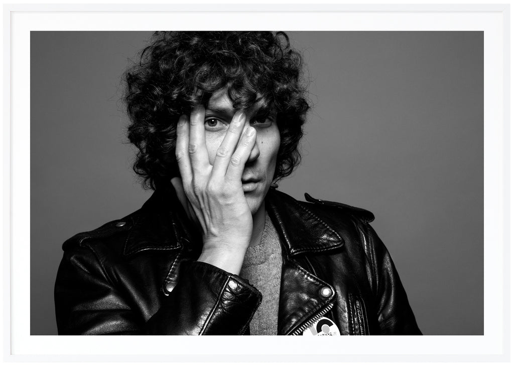 Håkan Hellström posts in black and white with one hand on his face. White frame. 