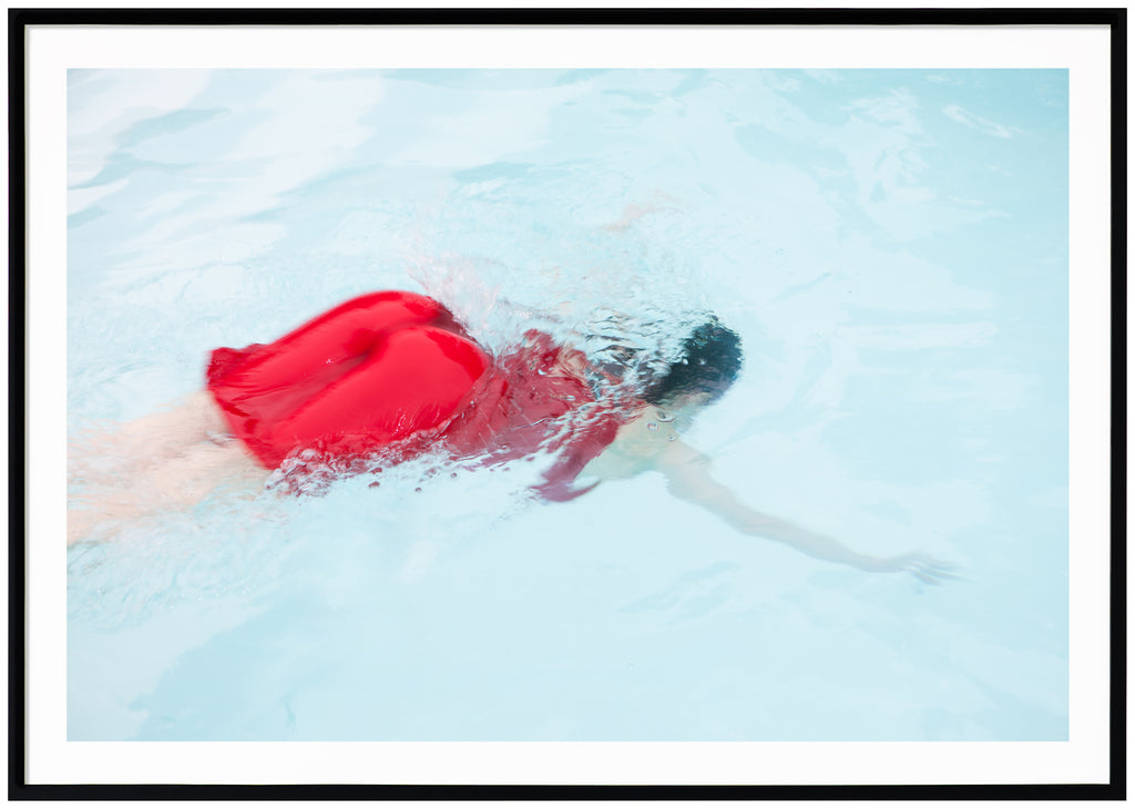 Poster of woman in red dress diving into light blue pool. Black frame. 