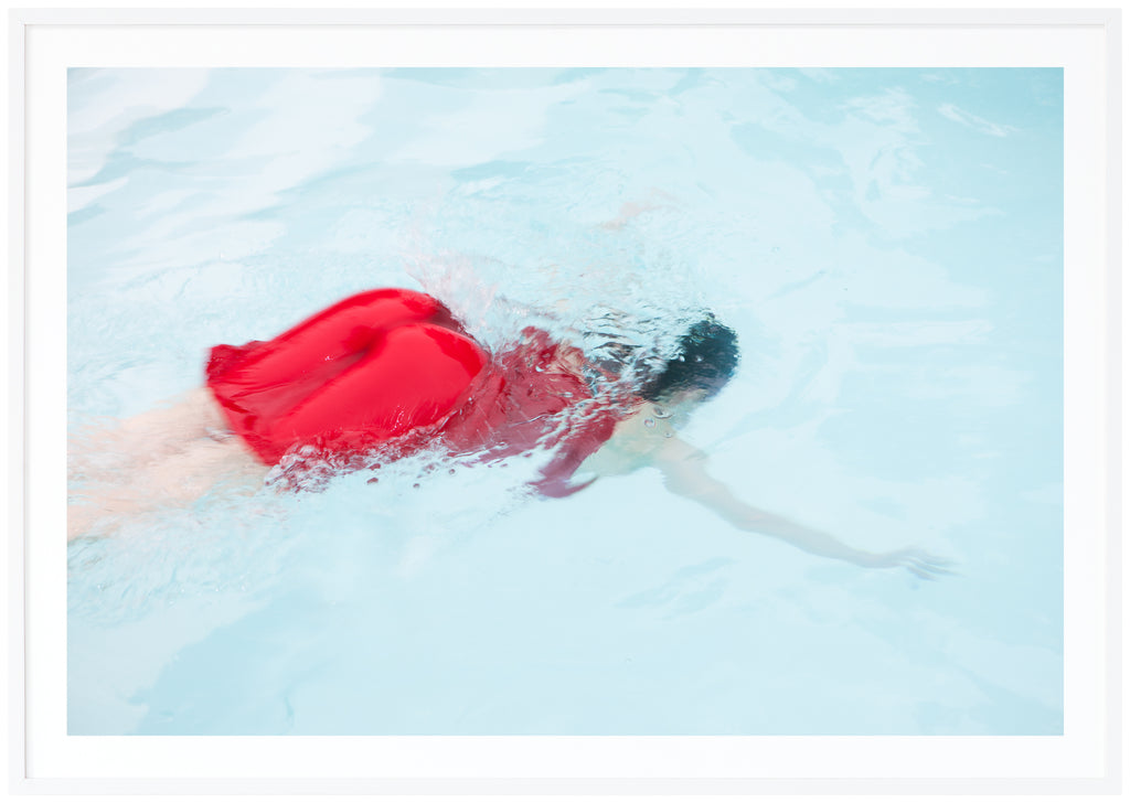 Poster of woman in red dress diving into light blue pool. White frame. 