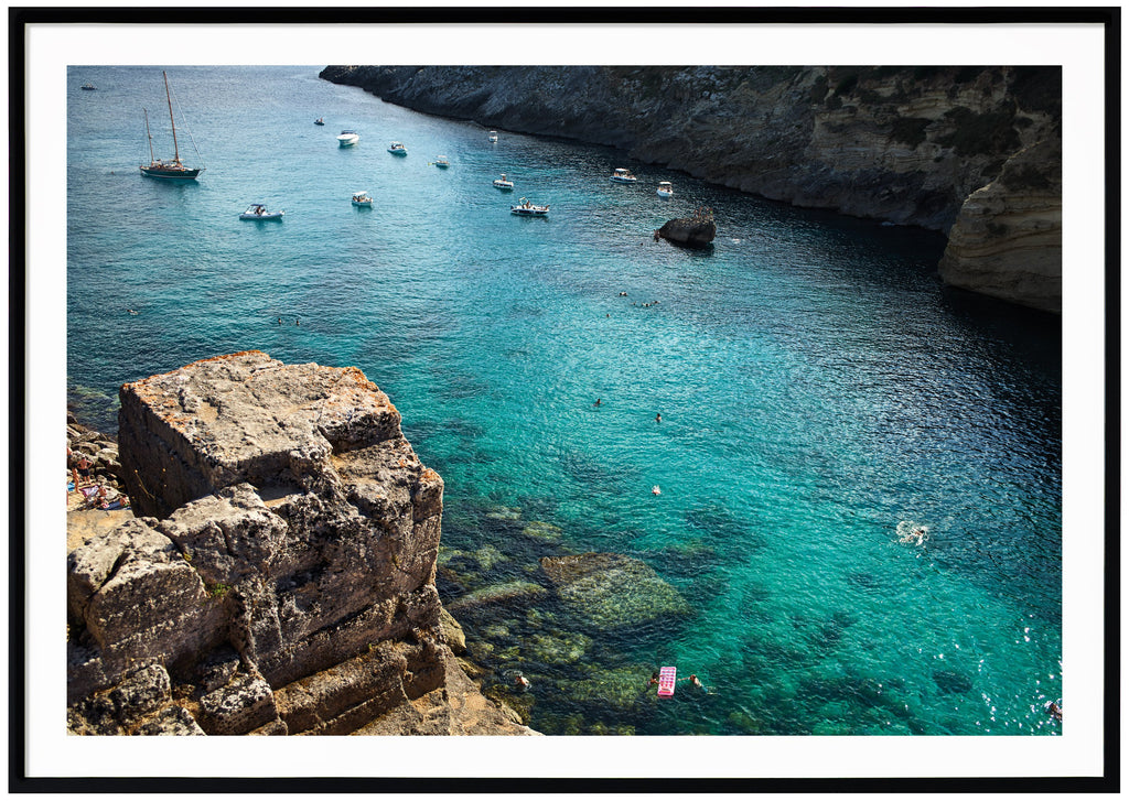 Photograph of cliffs, boats and the light blue Adriatic Sea in southern Italy.. Black frame. 