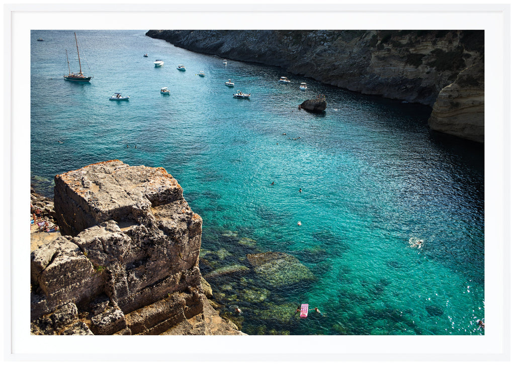Photograph of cliffs, boats and the light blue Adriatic Sea in southern Italy. White frame.