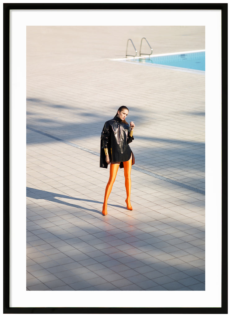 Woman wearing a pair of high orange Balenciaga boots near a swimming pool. Black frame. 