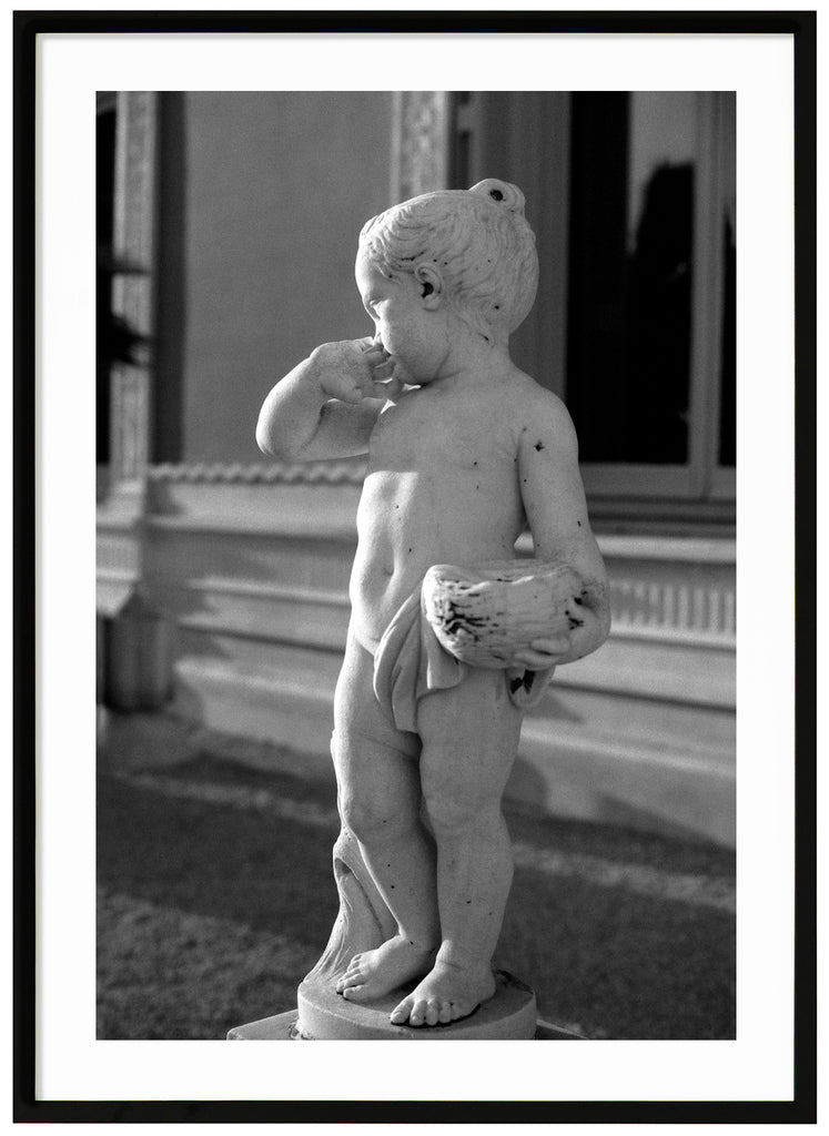 Black and white analog poster of small statue in garden. Background of a house. Black frame. 
