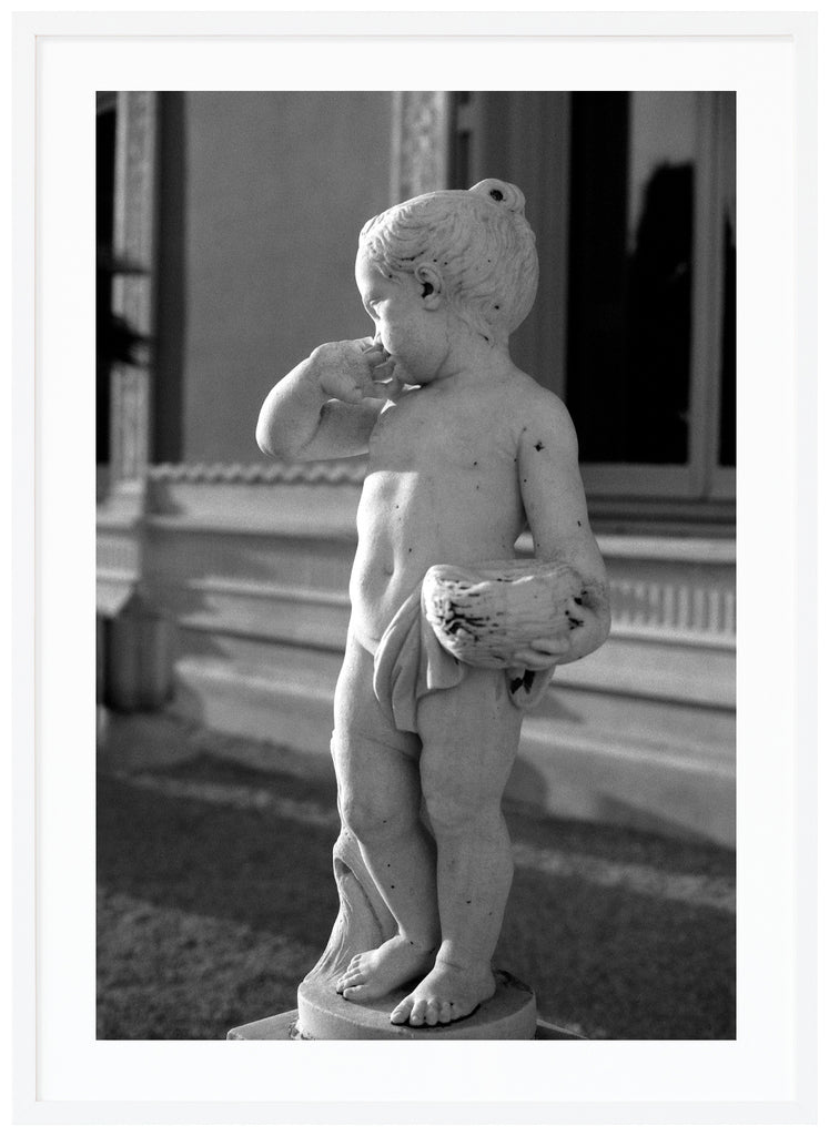 Black and white analog poster of small statue in garden. Background of a house. White frame. 