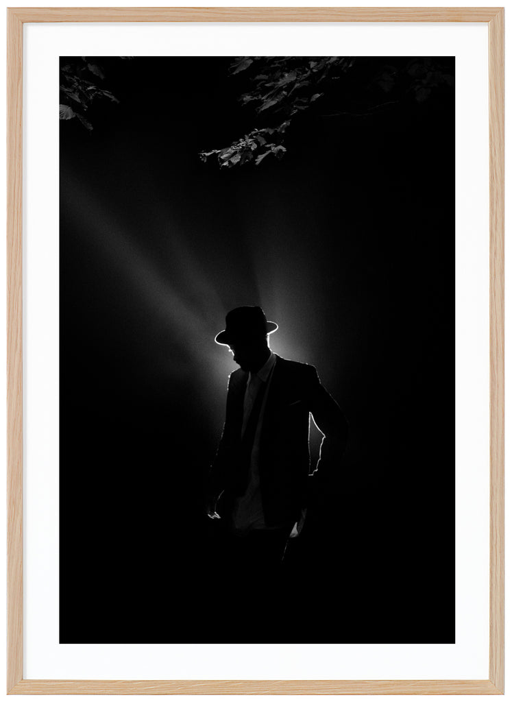 Black and white poster of a man illuminated from behind in suit and hat under some tree branches. Oak frame. 