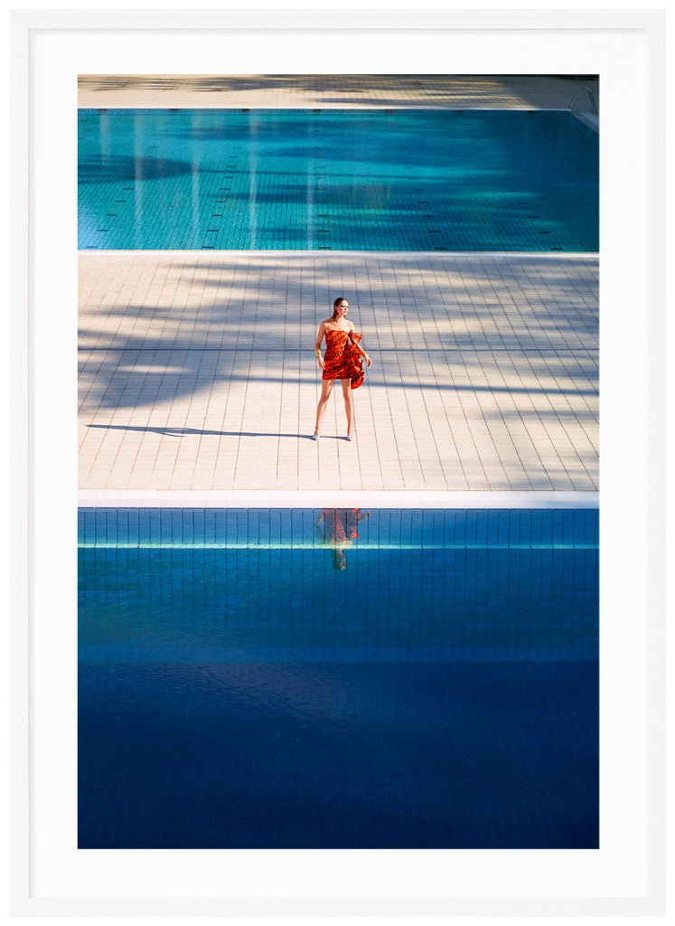 ConfusedPoster of woman in orange dress standing alone between two large swimming pools. White frame. 