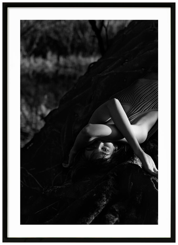 Black and white poster of woman lying on a tree. Black frame.