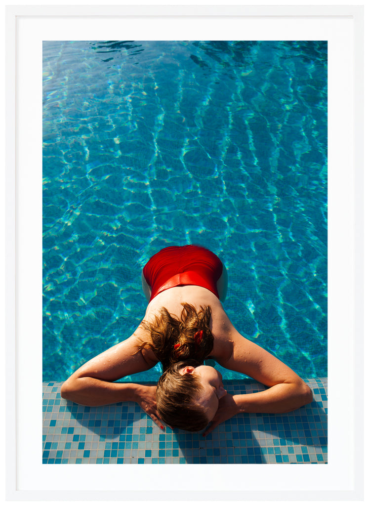Poster of woman in red swimsuit lying on poolside. White frame. 
