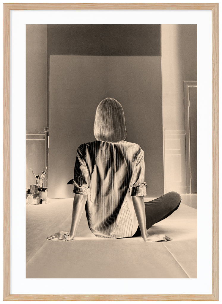 Monochrome photograph of a woman sitting in front of a blank canvas intended for painting. Oak frame. 