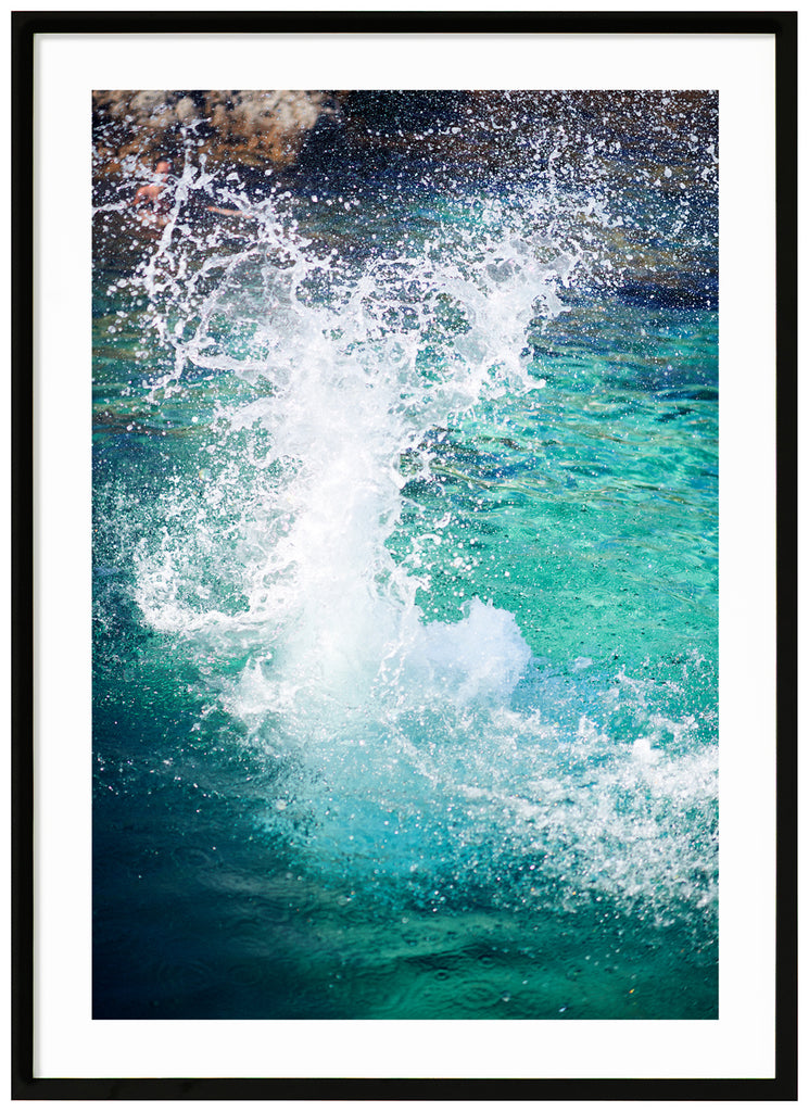 Color photography on light blue water hitting the rocks in the background. Black frame. 
