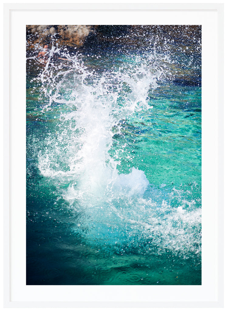 Color photography on light blue water hitting the rocks in the background. White frame. 