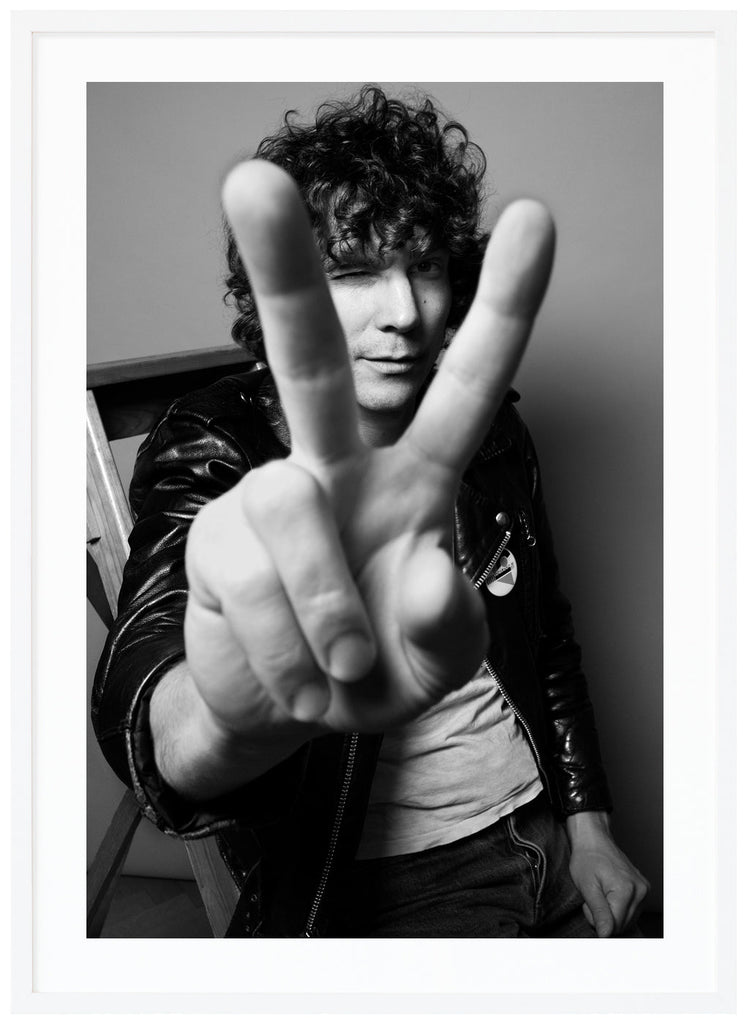 Håkan is holding upp two fingers to the camera. White frame. 