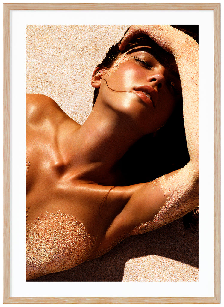 Photograph of a posed woman lying on her back with sand on her body.  Oak frame. 