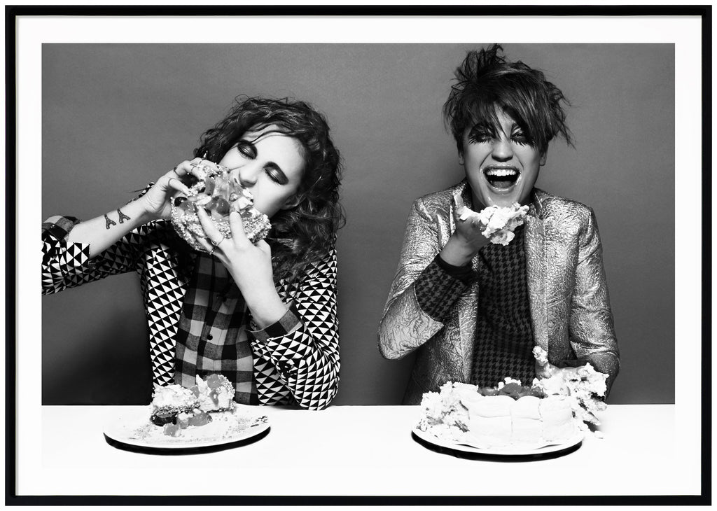 Black and white poster of icona pop eating cake. Black frame. 