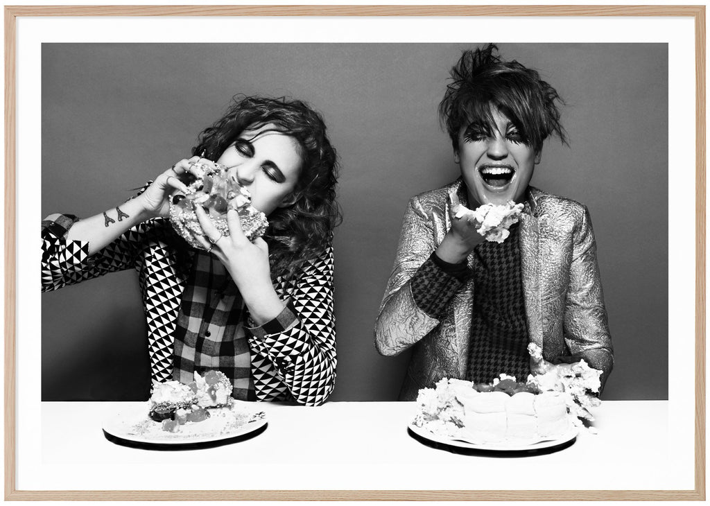 Black and white poster of icona pop eating cake. Oak frame. 