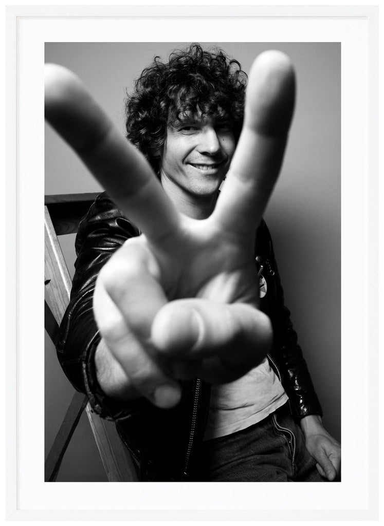 We see our Håkan holding up a peace sign with his fingers in front of the camera. White frame. 
