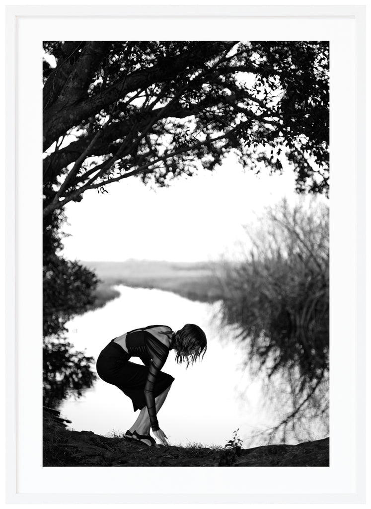 Black and white photograph of a woman under a tree with water in the background.  White frame. 