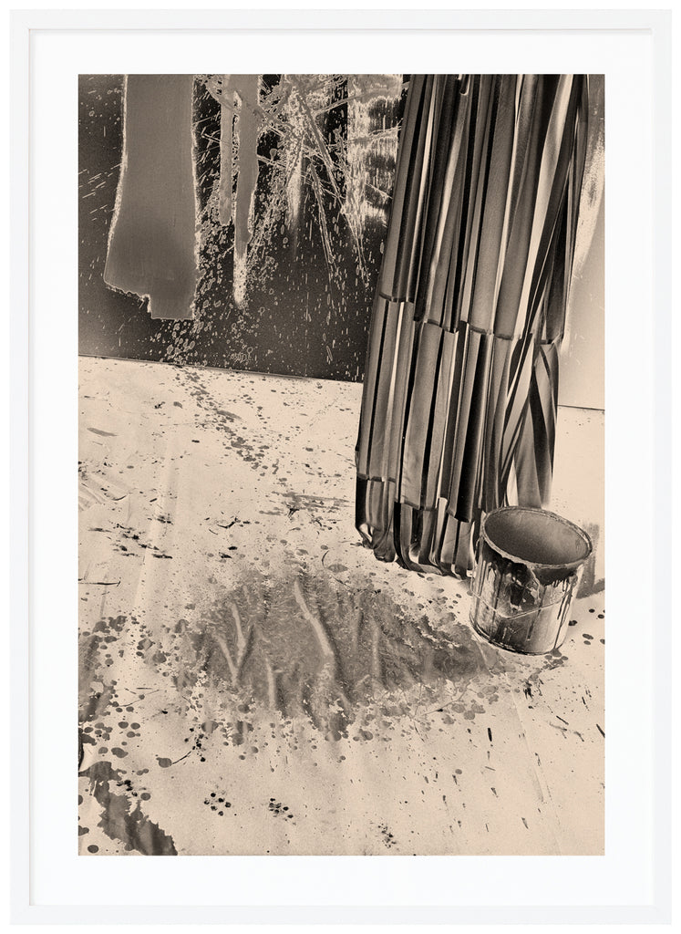 Monochrome photography in a warm tone of a paint bucket and paint splashes on the wall.  White frame. 