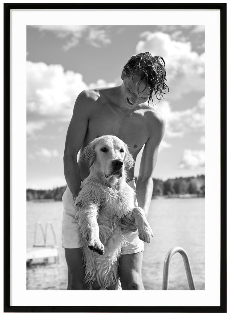 Black and white photograph of a man holding a dog standing on two legs. Black frame. 
