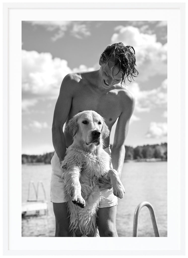 Black and white photograph of a man holding a dog standing on two legs. White frame. 