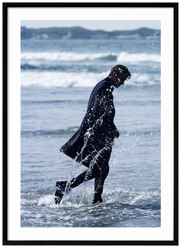 Poster of man in coat walking in the sea. Portrait format. Black frame.