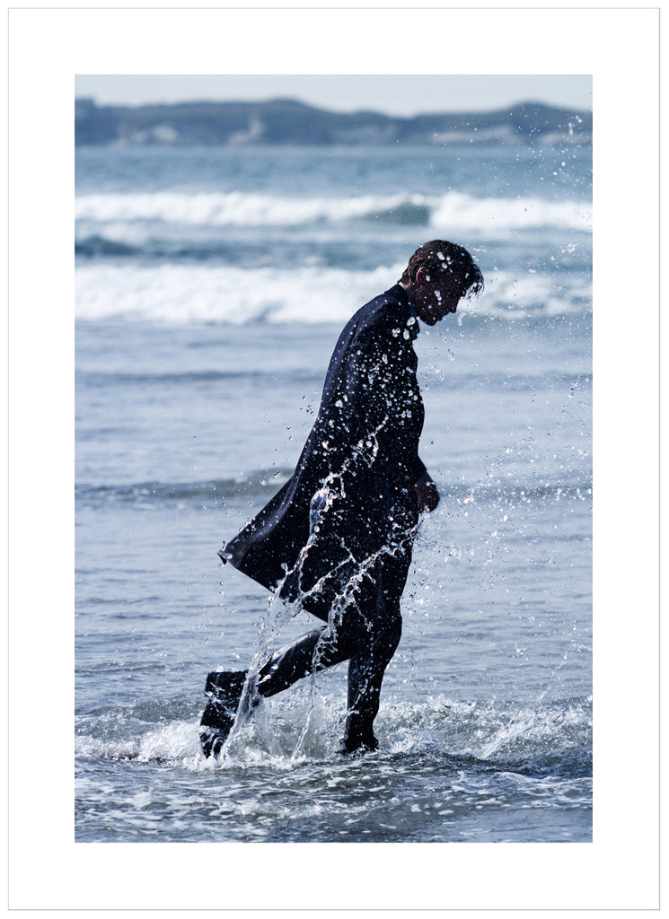 Poster of man in coat walking in the sea. Portrait format.