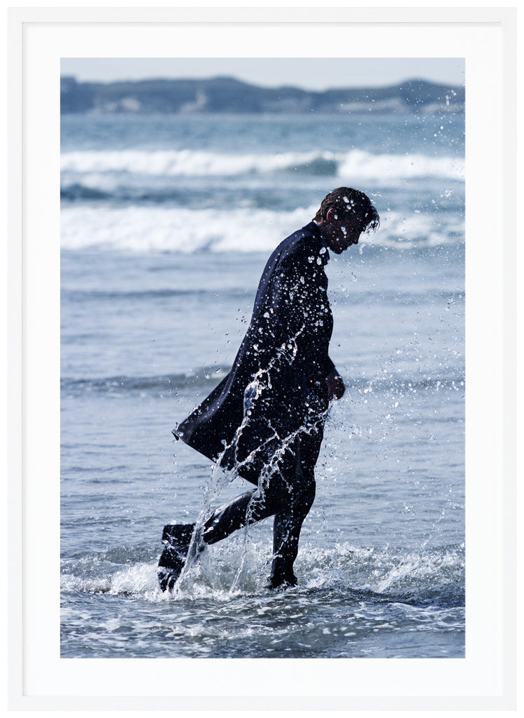 Poster of man in coat walking in the sea. Portrait format. White frame. 