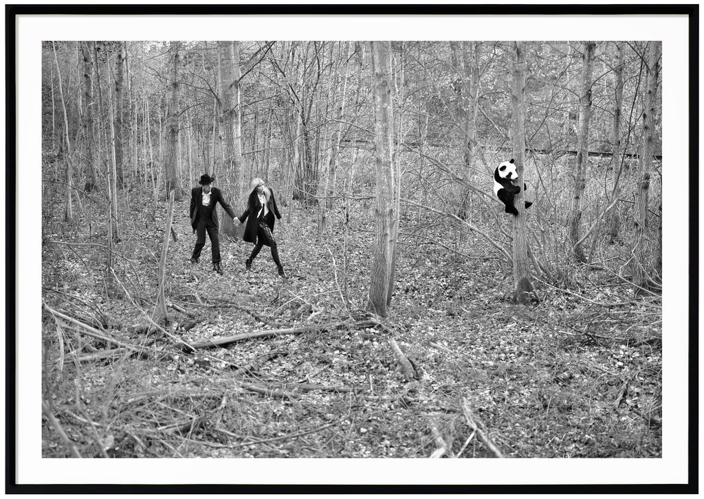 Analogous black and white photograph of a couple discovering a panda in a forest. Black frame. 