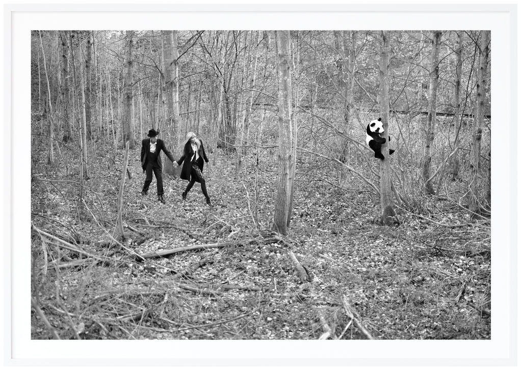 Analogous black and white photograph of a couple discovering a panda in a forest. White frame. 