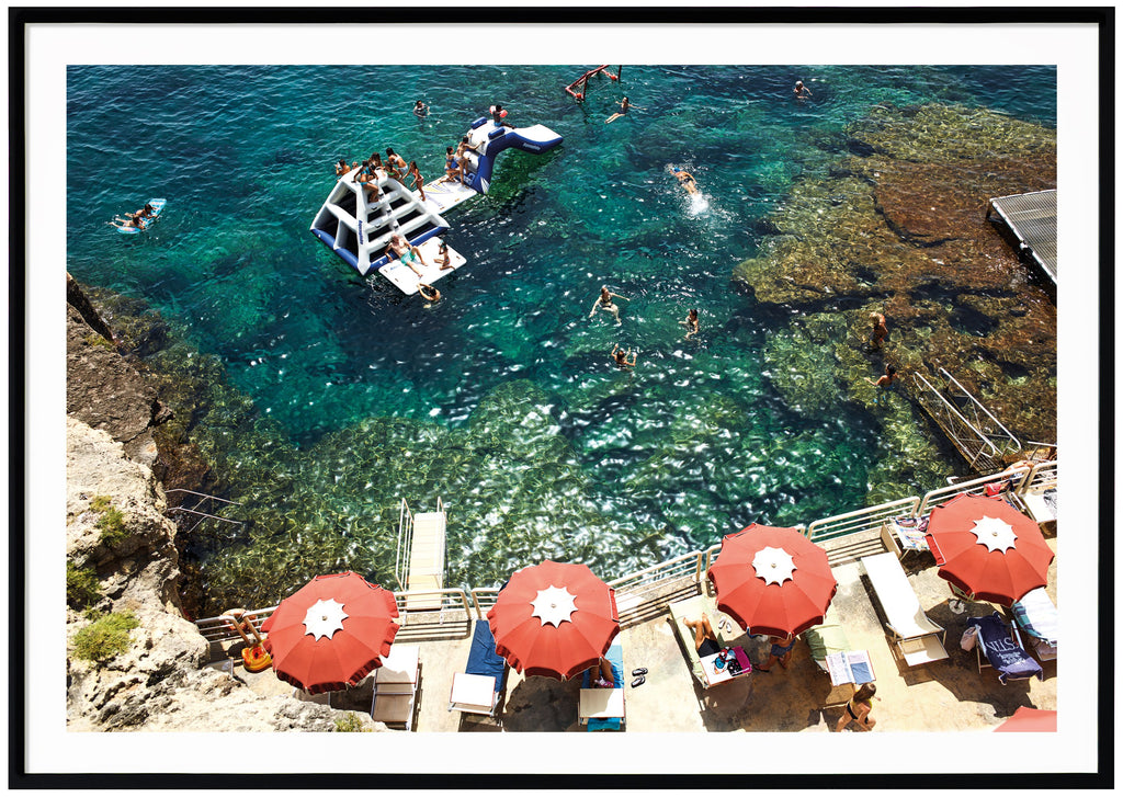 Records of bathing place in Italy. Red parasol. Children playing in the water on bouncy castle and slide. Black frame. 