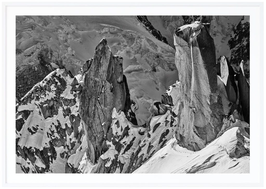 Black and white photograph of steep cliffs partly covered by snow.  White frame. 