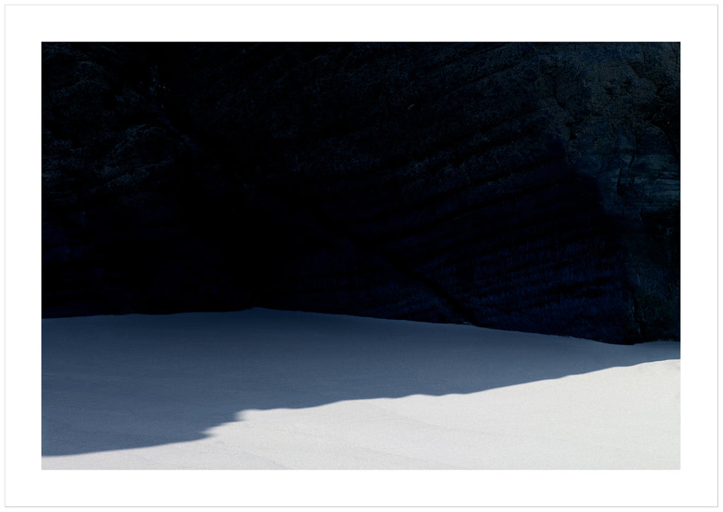  Graphic photograph of a beach with a shadow from a dark cliff. 