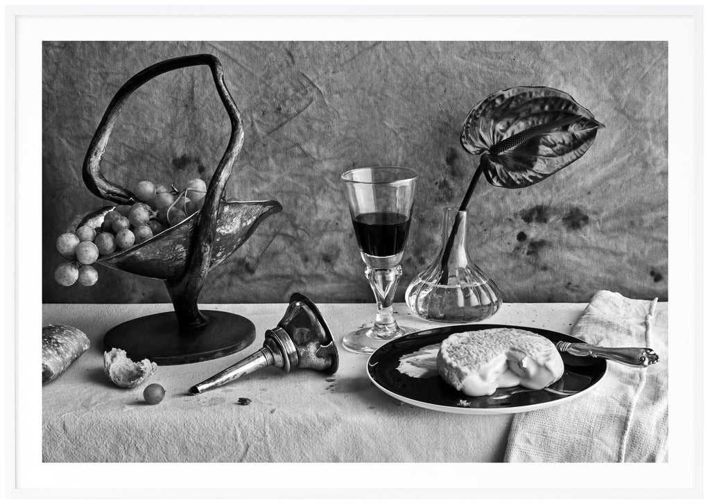  Still life in black and white of a table set with cheese and wine. White frame. 