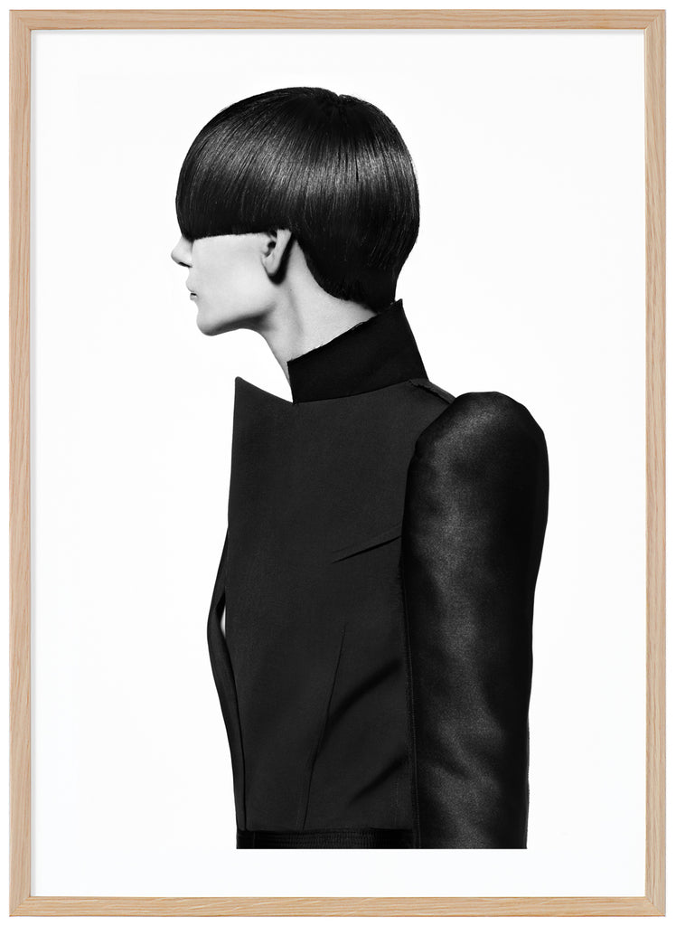 Black-and-white photograph of a female model with a bob-like hairstyle and wearing a black coat. Oak frame. 