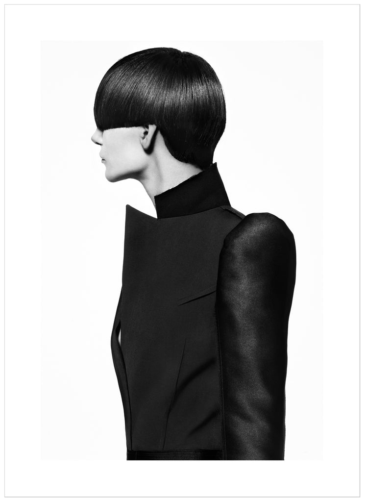Black-and-white photograph of a female model with a bob-like hairstyle and wearing a black coat.