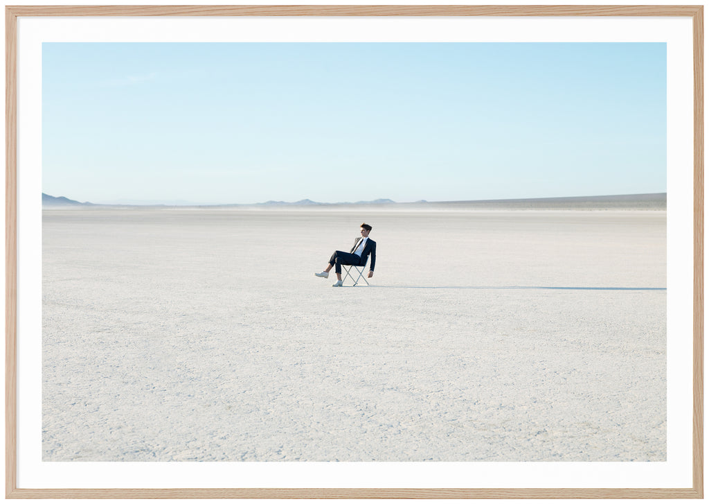 Photograph of costumed man sitting on a chair in the Mojave Desert, California.  Oak frame.