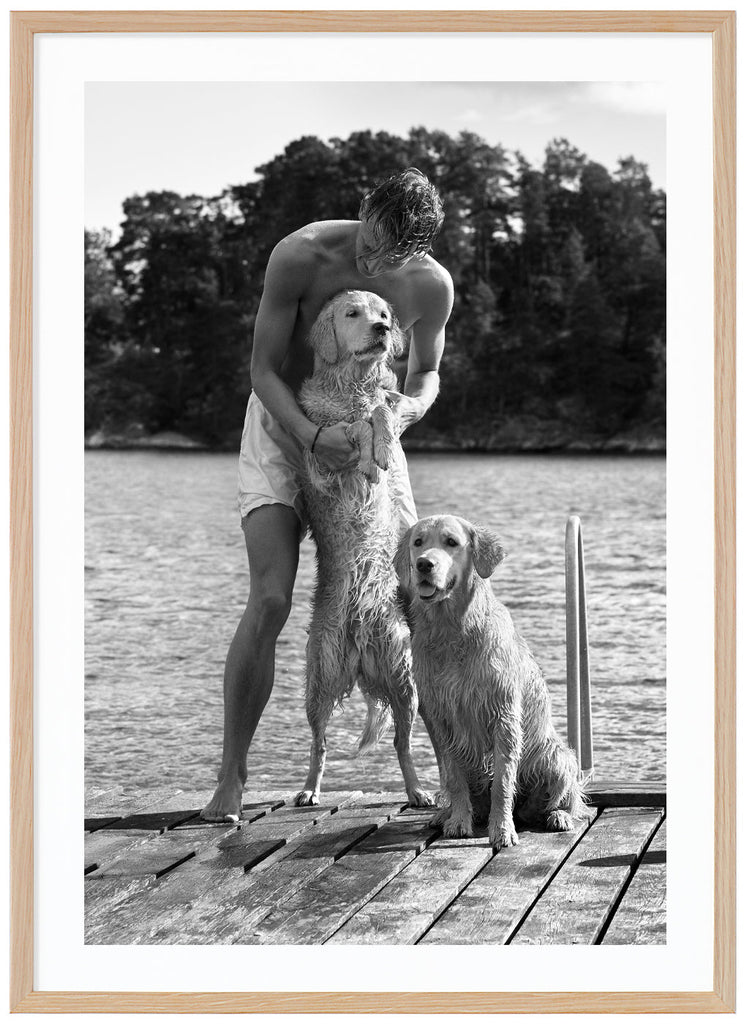 Black and white poster of guy with dogs on a wet jetty. Portrait format. Oak frame. 