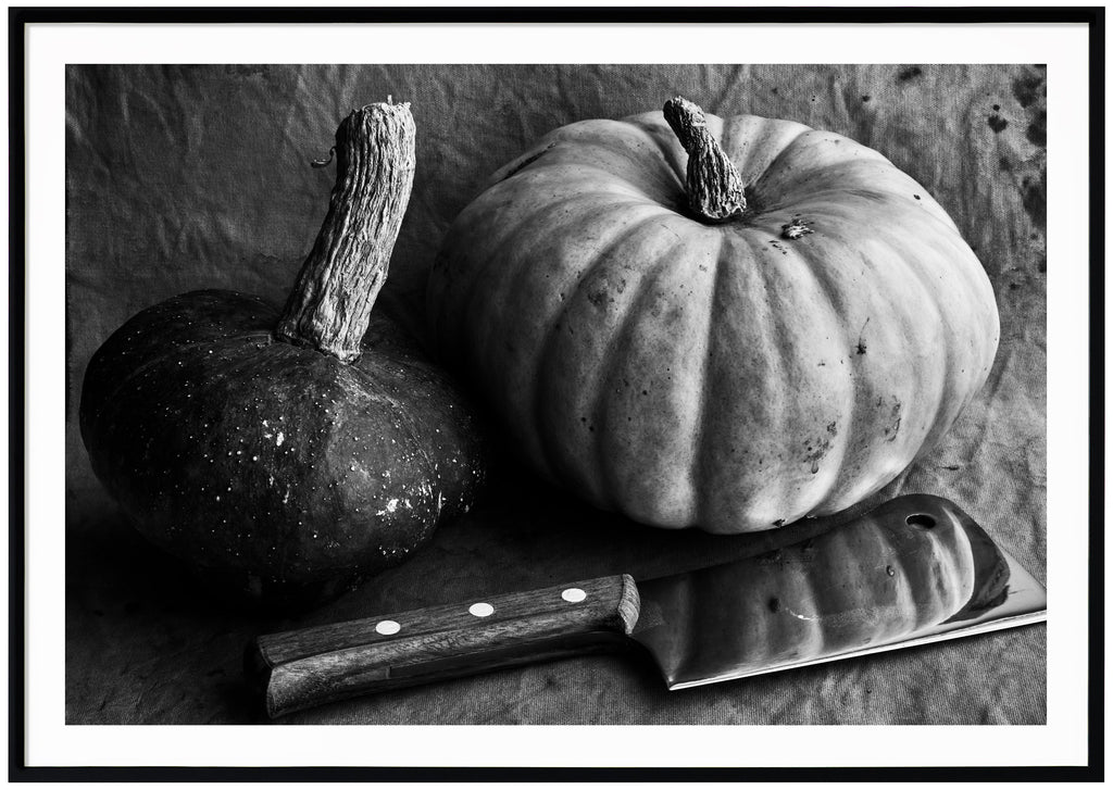 Black and white still life of two pumpkins and a meat ax. Black frame. 