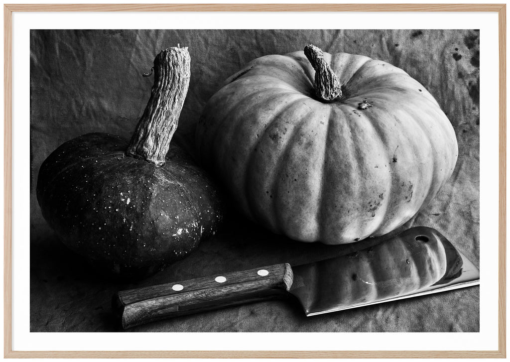 Black and white still life of two pumpkins and a meat ax. Oak frame.