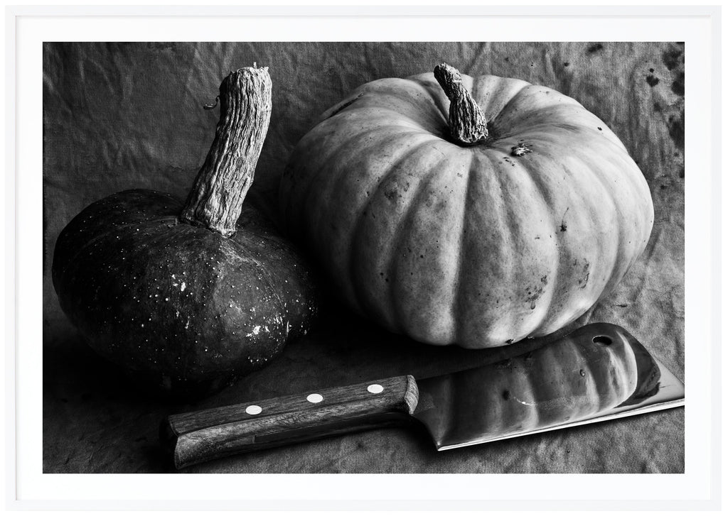 Black and white still life of two pumpkins and a meat ax. White frame. 