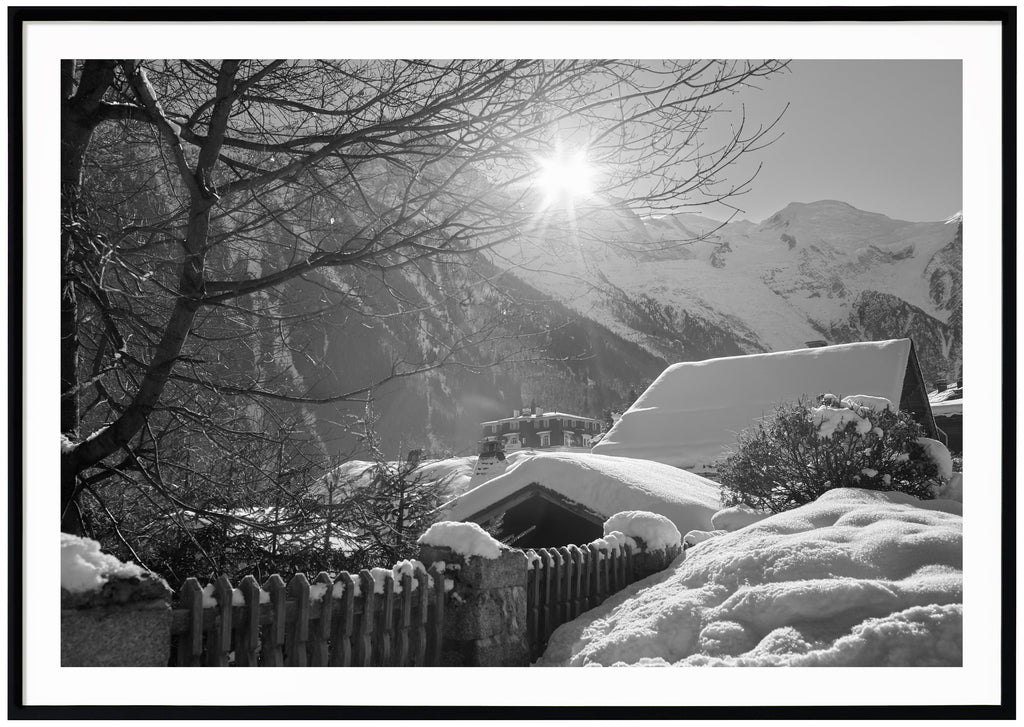 Black and white photograph of snow-covered rooftops with alps in the background. Black frame.
